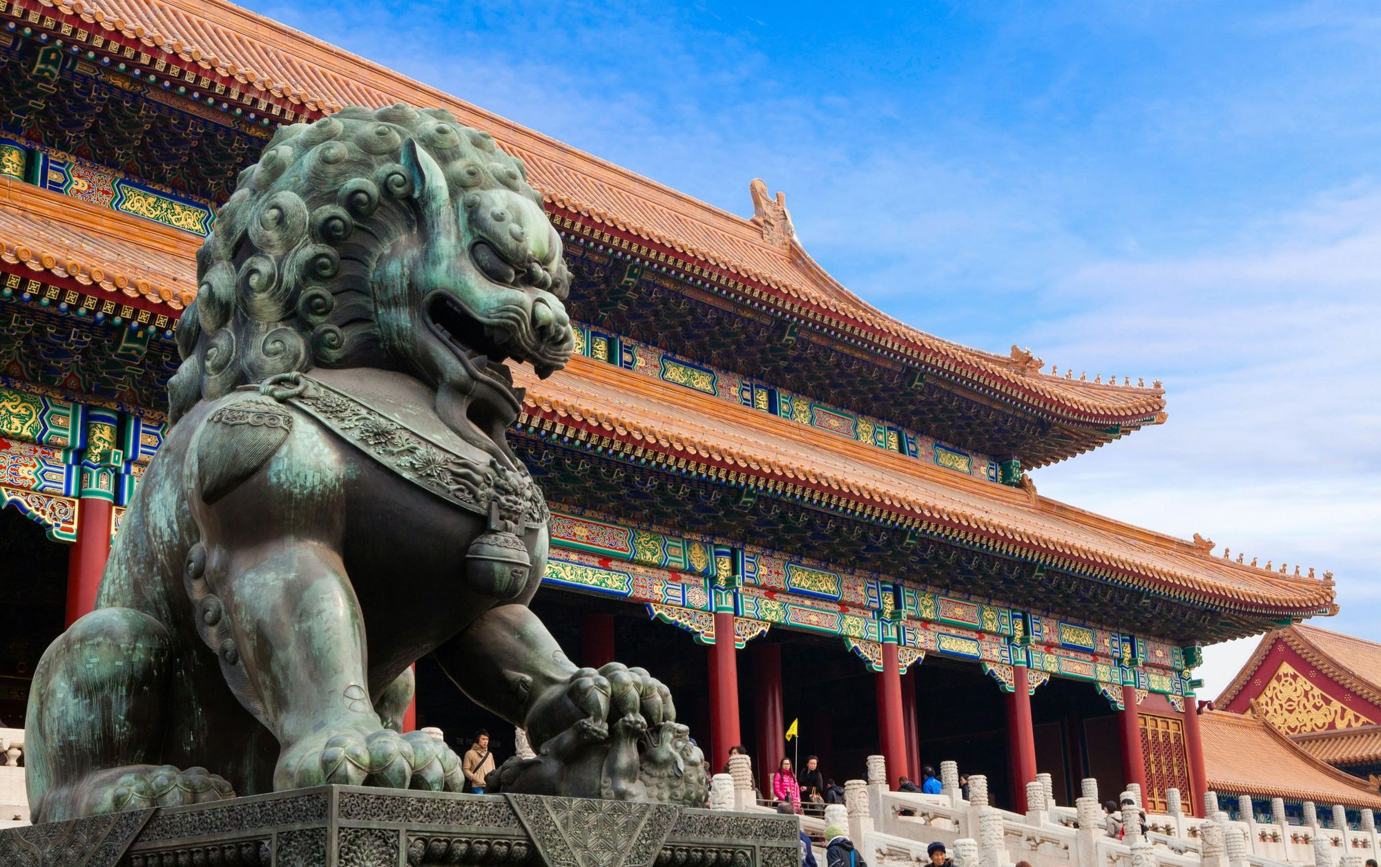 A bronze guardian lion in front of a hall of the Forbidden City in Beijing, under a clear blue sky